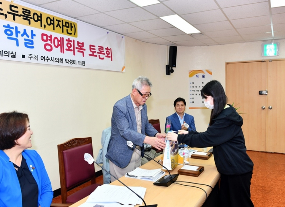 ▲지난해 6월 여수시의회에서 열린 ‘한국전쟁기(이야포, 두룩여, 여자만) 미군폭격 민간인 학살 명예회복 토론회’ 모습. 토론회를 방청한 학생이 이야포 학살 생존자인 이춘혁 어르신에게 꽃다발을 전하고 있다