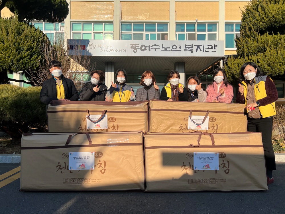 ▲복지관 앞에서 봉사자들이 전기장판을 두고 기념사진을 찍고 있다