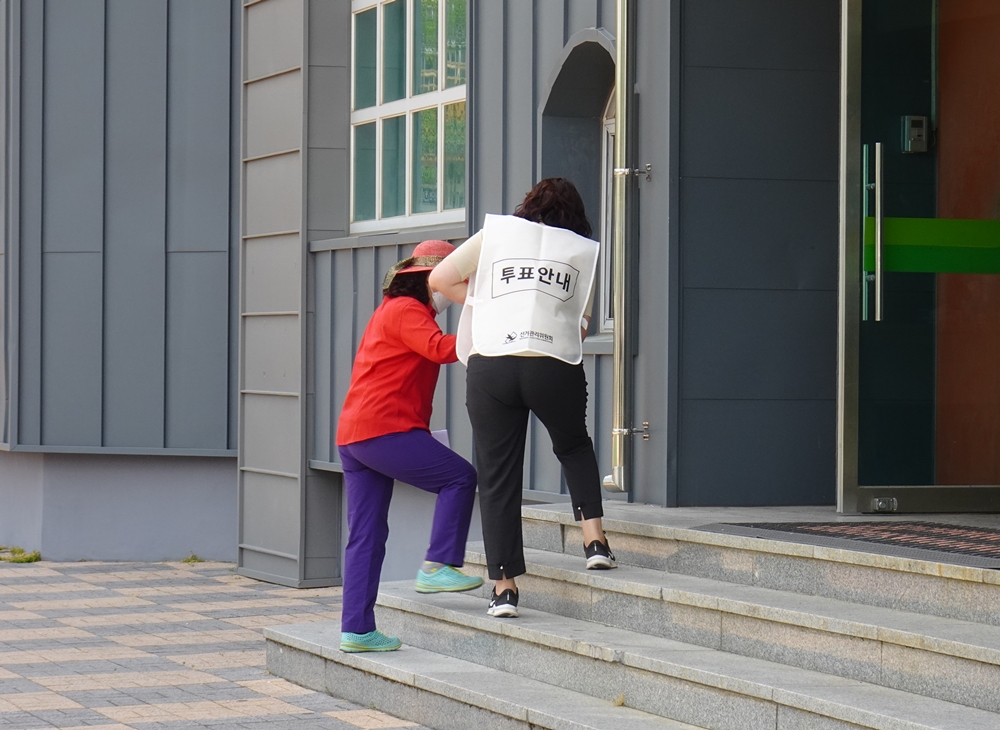 ▲ 투표안내원이 거동이 불편한 유권자를 부축하고 있다.