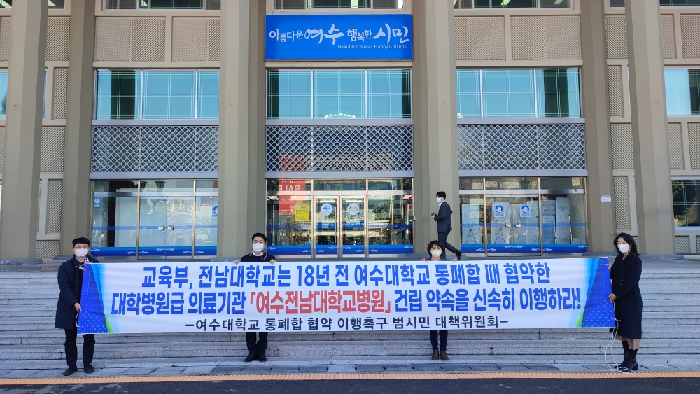 ▲지난 10일 여수시-민주당 당정협의회가 열린 여수시청 앞에서 여수대학교 통폐합협약 이행촉구 범시민대책위원회가 현수막을 들고 있다.