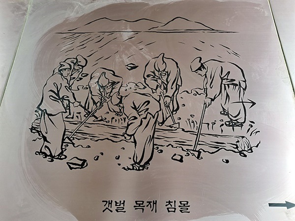 ▲   관음포광장에 새겨진 그림 속에 팔만대장경을 판각하기 전에 목재를 바다에 담그는 과정이 그려져 있다. 송화가루가 날려 보이지 않자 동행했던 남해군문화관광해설사 정영숙씨가 빗자루로 쓸고 걸레로 닦아줬다. 고마운 분이다 ⓒ오문수