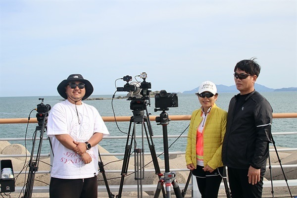 ▲  누리호 발사장면을 눈으로 직접 볼 수 있는 낭도 방파제에는 카메라가 50여대 설치되어 있었다. 유투브 명 '카메라에 담다' 김종관 감독은 "흔히 볼 수 있는 장면이 아닌 역사적 장면을 촬영하고 싶어서 3일째 여수에 머물고 있다"고 말했다. 서울에서 온 김성씨 부부가 발사장이 보이는 곳에서 김종관 감독과 기념촬영했다.ⓒ 오문수