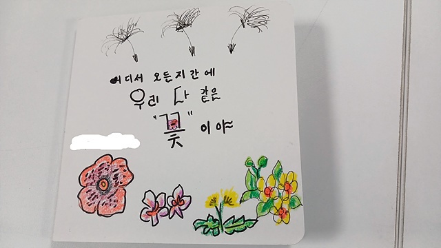 ▲8년전 한국으로 시집 온 인도네시아 여성이 그린 그림책 표지로 "어디서 오든지 간에 우리 다 같은 꽃이야"라는 글귀가 씌어있다. 인도네시아에는 민들레가 없다고 한다. 그녀의 설명에 의하면 한국에서 날아간 민들레 씨앗이 인도네시아에 핀 '라플레시아' 꽃과 인도네시아 국화인 쟈스민 꽃 옆으로 날아가고 있다. 아직은 이름을 밝히고 싶지 않다고 해서 그녀의 이름은 삭제했다 ⓒ오문수